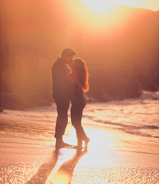 Pareja besándose en la playa a contraluz del atardecer